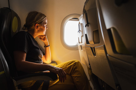 Happy passenger woman is flying in plane. Girl sitting in airplane looking out window going on trip vacation travel. Traveling female inside plane enjoying flight. Traveling girlの写真素材