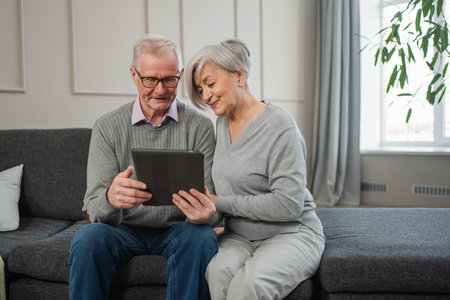 Senior old couple with tablet watching video online. Husband wife spending time together at home. Happy modern mature senior couple using tablet for family entertainment. Old people modern technologyの写真素材