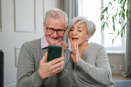 Video call. Happy senior couple woman man with smartphone having video call. Mature old grandmother grandfather talking speaking online. Older generation modern tech usage. Virtual meeting online chatの写真素材