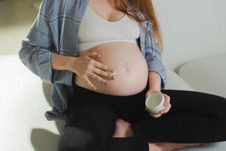 Pregnancy motherhood. Pregnant woman applying cream lotion on big belly takes care of her skin....