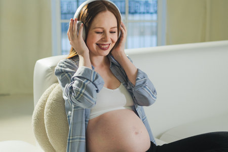 Pregnancy motherhood. Pregnant woman listening music for mother and unborn baby at home. Girl in headphones enjoying pregnancy listen music for relax healthy zen calm peace wellness, Maternity conceptの写真素材