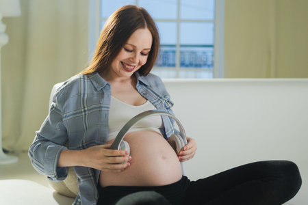Pregnancy motherhood. Pregnant woman holding headphones near belly listening music for mother and unborn baby. Girl enjoying pregnancy listen music for relax calm wellness. Prenatal music stimulationの写真素材