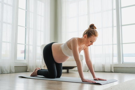 Pregnancy yoga fitness workout training. Pregnant woman practicing yoga at home. Pregnant girl doing sports exercise on yoga mat indoor. Woman with big belly have fitness training practicing asanaの写真素材