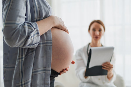 Pregnant woman hands touching big belly in doctor office. Female doctor examining pregnant woman. Gynecologist doctor consulting patient about pregnancy in hospital. Visit to doctor medical checkupの写真素材