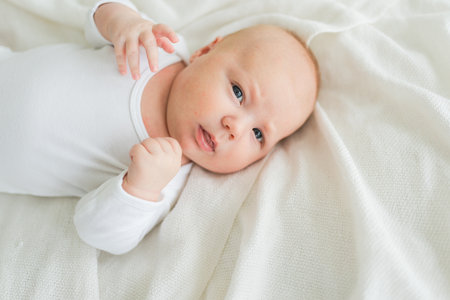 Happy baby. Cute little newborn girl with smiling face lying on bed in bedroom. Infant baby resting playing lying down on white blanket at home. Motherhood happy child childcare conceptの写真素材