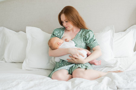 Happy family at home. Mother breastfeeding baby for health nutrition wellness. Mom nursing feeding her newborn child milk at home. Woman infant girl in white bedroom Mother hugs baby with love careの写真素材