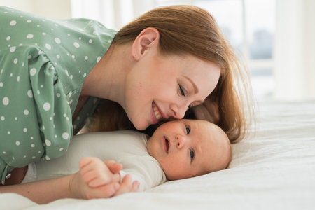 Happy family at home. Mother playing with little toddler child on bed. Mom baby relax playing having...