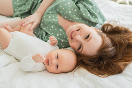 Happy family at home. Mother playing with little toddler child on bed. Mom baby relax playing having fun together. Mother looks at camera with love care. Mom of baby rest in living roomの写真素材