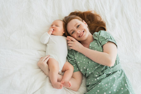 Happy family at home. Mother playing with little toddler child on bed. Mom baby relax playing having fun together. Mother looks at camera with love care. Mom of baby rest in living roomの写真素材