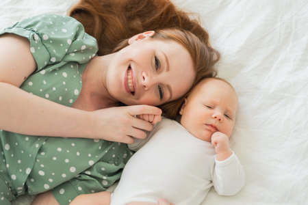 Happy family at home. Mother playing with little toddler child on bed. Mom baby relax playing having fun together. Mother looks at camera with love care. Mom of baby rest in living roomの写真素材
