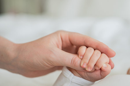 Happy family. Tiny newborn infant baby little hand on mother hand palm. Newborn baby holding parent finger after birth. Mom baby at home. Support protection of new life. Handle with careの写真素材