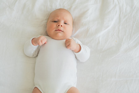 Happy baby. Cute little newborn girl with smiling face lying on bed in bedroom. Infant baby resting playing lying down on white blanket at home. Motherhood happy child childcare conceptの写真素材
