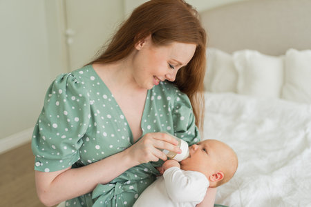 Happy family at home. Mother holding little baby toddler child feeding milk from bottle. Newborn Infant baby girl sucking eating drinking milk. Mom of breast feeding baby. Motherhood happy childの写真素材