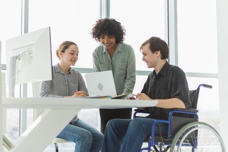Teamwork brainstorm. Diverse multiracial colleagues man in chair for people with disability working together. Group of people sitting in creative office discussing business. Young professional teamの写真素材