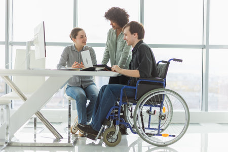 Teamwork brainstorm. Diverse multiracial colleagues man in chair for people with disability working together. Group of people sitting in creative office discussing business. Young professional teamの写真素材