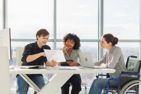 Teamwork brainstorm. Diverse multiracial colleagues woman in chair for people with disability working together. Group of people sitting in creative office discussing business. Young professional teamの写真素材