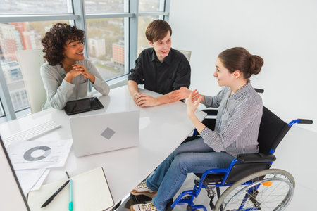 Teamwork brainstorm. Diverse multiracial colleagues woman in chair for people with disability working together. Group of people sitting in creative office discussing business. Young professional teamの写真素材