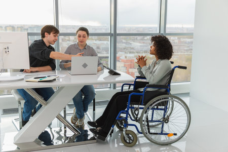 Teamwork brainstorm. Diverse multiracial colleagues woman in chair for people with disability working together. Group of people sitting in creative office discussing business. Young professional teamの写真素材