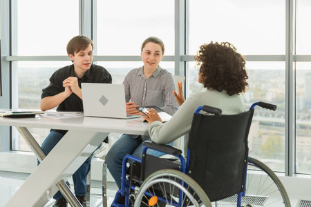 Teamwork brainstorm. Diverse multiracial colleagues woman in chair for people with disability working together. Group of people sitting in creative office discussing business. Young professional teamの写真素材