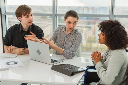 Teamwork brainstorm. Diverse multiracial colleagues woman in chair for people with disability working together. Group of people sitting in creative office discussing business. Young professional teamの写真素材