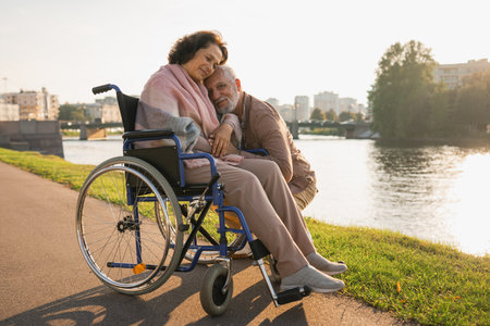 Senior woman in wheelchair walking with caregiver old man on road. Elderly family couple man supporting taking care of paralyzed woman in chair for people with disability outdoor. Rehabilitationの写真素材