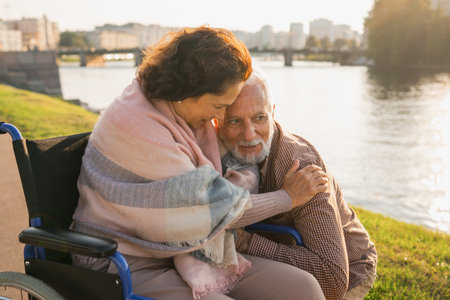 Senior woman in wheelchair embracing elderly man in park. Elderly family couple supporting each other for people with disability outdoor. Rehabilitationの写真素材