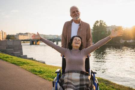 Senior woman in wheelchair walking with caregiver old man on road. Family couple man husband supporting taking care of paralyzed woman wife in chair for people with disability outdoor. Rehabilitationの写真素材