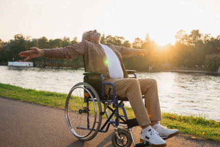 Happy senior man in wheelchair raised hands enjoying freedom walking on road in city park outdoor. Old happy man in chair for people with disability has a hope. Disability disease rehabilitationの写真素材