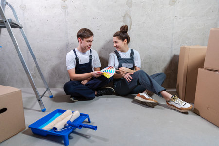 House decoration DIY renovation concept. Happy couple sitting on floor in empty room of new home planning design. Husband and wife holding swatch palette choosing colors for painting wall in new houseの写真素材