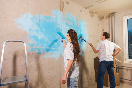 Couple in new home during repair works painting wall together. Happy family holding paint roller painting wall with blue color paint in new house. Home renovation DIY renew home conceptの写真素材
