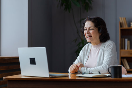 Happy middle aged senior woman sit with laptop talk on video call with friends family. Laughing mature old senior grandmother having fun talking speaking with grown up children onlineの写真素材