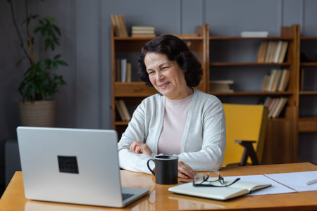 Happy middle aged senior woman sit with laptop talk on video call with friends family. Laughing mature old senior grandmother having fun talking speaking with grown up children onlineの写真素材