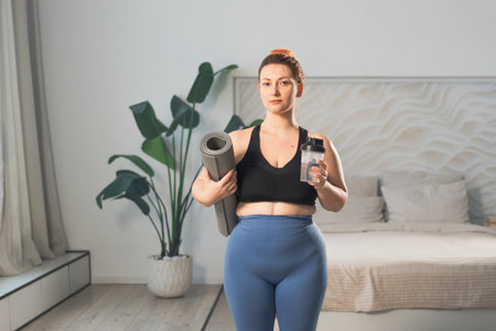 Yoga fitness sport workout training. Woman hold yoga mat bottle water ready for practicing yoga at home. Plus size female doing sports indoor. Girl in sportswear have training workout for weight lossの写真素材