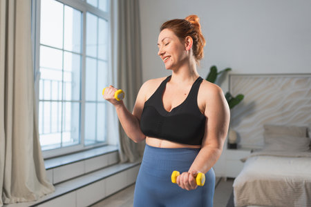 Fitness workout training. Woman picking up dumbbells. Plus size female doing sports exercise at home indoor. Girl in sportswear have workout weight training for weight loss. Sport and fitnessの写真素材