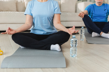 Yoga mindfulness meditation. Senior mature couple practicing yoga at home. Hands in chin mudra gesture. Old husband wife sitting in lotus pose meditating relaxing. Family doing breathing practice.の写真素材