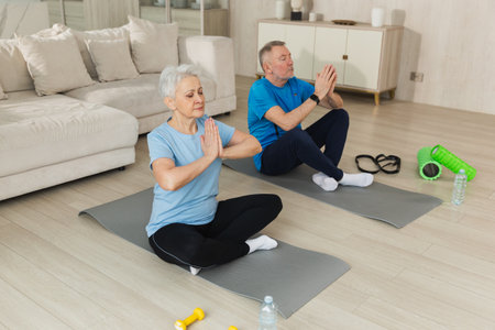 Yoga mindfulness meditation. Senior adult mature couple practicing yoga at home. Mid age old husband wife sitting in lotus pose on yoga mat meditating relaxing. Family doing breathing practiceの写真素材