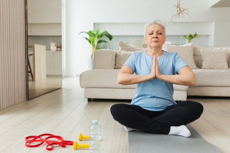 Yoga mindfulness meditation. Senior adult mature woman practicing yoga at home. Mid age old lady sitting in lotus pose on yoga mat meditating relaxing. Older middle aged woman doing breathing practiceの写真素材