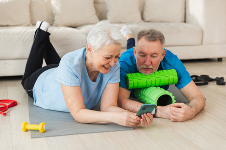 Yoga fitness training online. Senior couple practicing yoga fitness with online lessons on smartphone. Old wife husband watching training on phone before workout. Family doing sports exercise at homeの写真素材