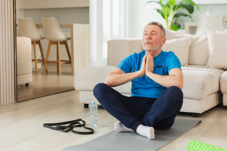Yoga mindfulness meditation. Senior adult mature man practicing yoga at home. Mid age old grandfather sitting in lotus pose on yoga mat meditating relaxing. Older man doing breathing practiceの写真素材
