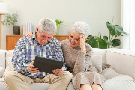 Senior old couple with tablet watching video online. Husband wife spending time together at home. Happy modern mature senior couple using tablet for family entertainment. Old people modern technologyの写真素材