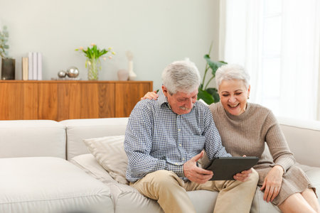 Senior old couple with tablet watching video online. Husband wife spending time together at home. Happy modern mature senior couple using tablet for family entertainment. Old people modern technologyの写真素材