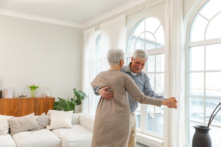Keep moving. Romantic senior mature couple dancing to music together at home. Happy smiling family retired man woman husband wife having fun enjoying time together. Family moment love careの写真素材