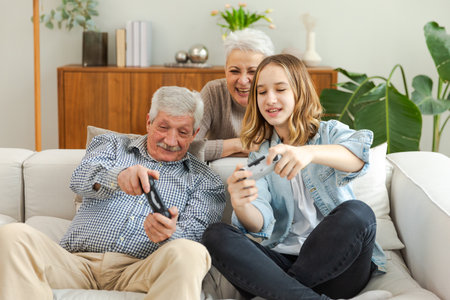 Happy family at home. Old senior man grandfather woman grandmother girl granddaughter playing video game with joysticks at home. Grandparent teenager two generations using gamepads for video gameの写真素材