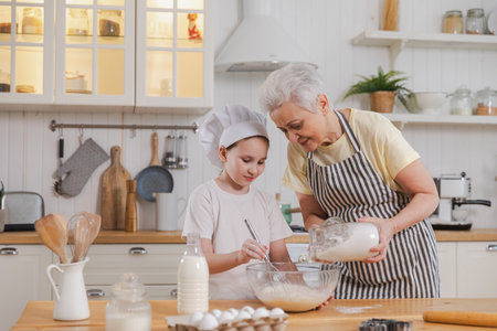 Happy family in kitchen. Grandmother and granddaughter child cook in kitchen together. Grandma teaching kid girl knead dough bake cookies. Household teamwork helping family generations conceptの写真素材
