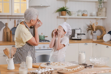 Happy family in kitchen. Grandmother granddaughter child cutting cookies of dough on kitchen table together. Grandma teaching kid girl cook bake cookies. Household teamwork helping family generationsの写真素材