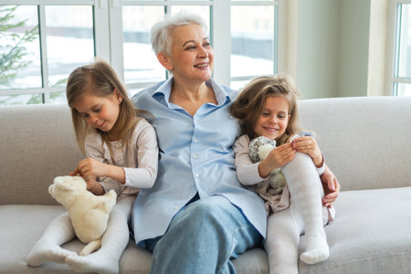Happy family at home. Two little girls sisters twins grandmother enjoying time together. Good time at home. Grandma granddaughters child kids emotional bonding hugging together. Family generationsの写真素材