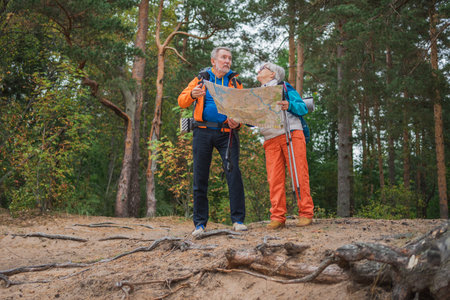 Hiking tourism. Senior couple man woman looking track in paper map enjoying hiking in forest. Happy...