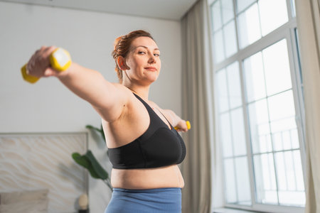 Fitness workout training. Woman picking up dumbbells. Plus size female doing sports exercise at home...
