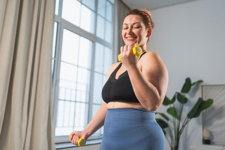 Fitness workout training. Woman picking up dumbbells. Plus size female doing sports exercise at home...