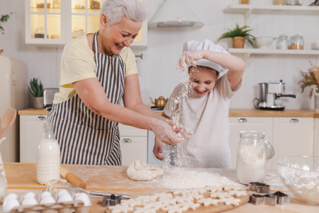 Happy family in kitchen. Grandmother and granddaughter child cook in kitchen together. Grandma teaching kid girl knead dough bake cookies. Household teamwork helping family generations conceptの写真素材